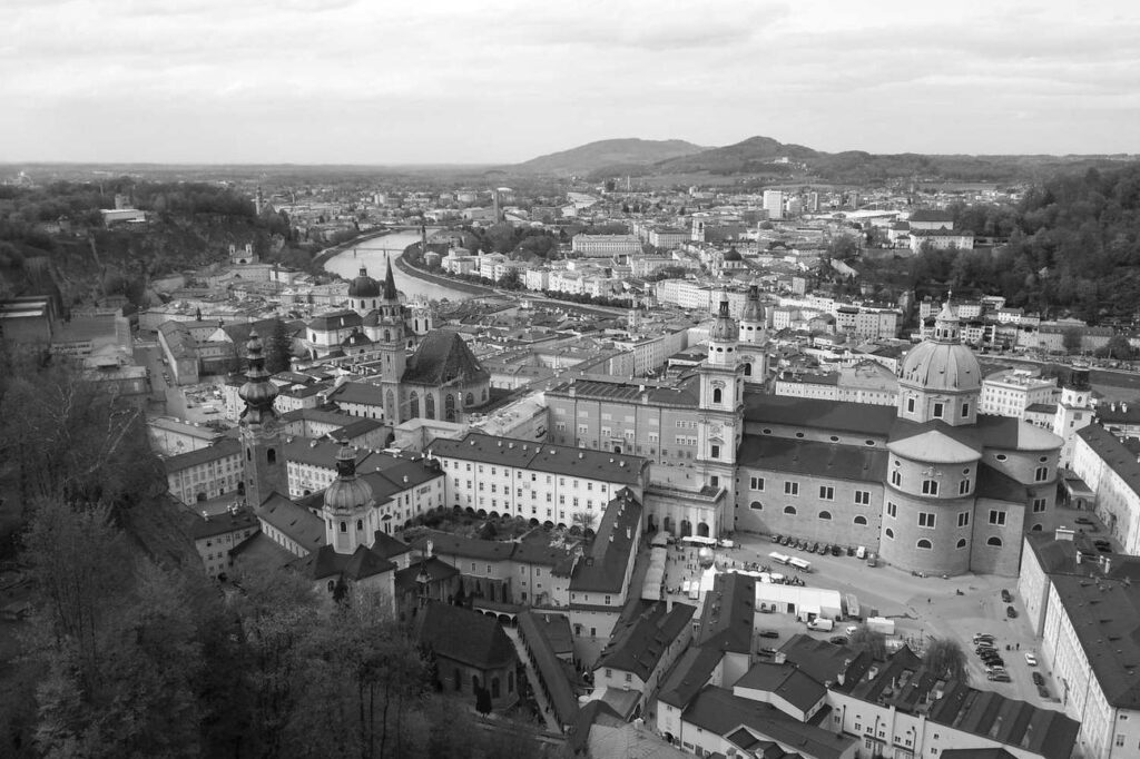 Luftaufnahme einer historischen europäischen Stadt mit alten Gebäuden, Kuppelkirchen und einem Fluss, der sich durch die Stadt schlängelt, umgeben von Hügeln und Bäumen.